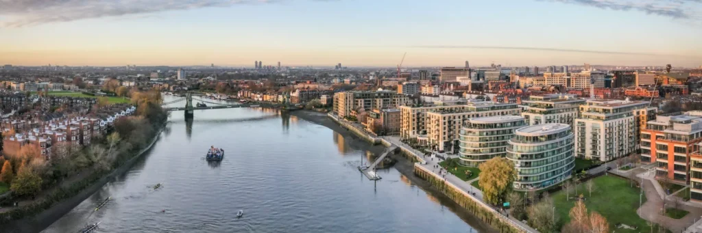 Aerial view of Fulham and Hammersmith riverside, featuring luxury developments, the Thames, Hammersmith Bridge, and the London skyline at sunset.