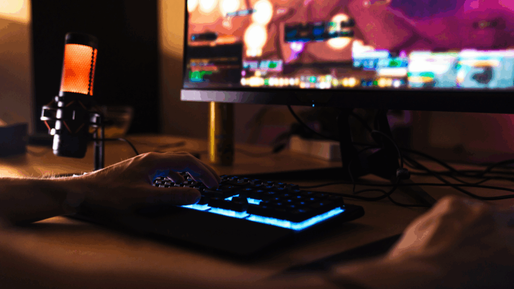 Cropped image of caucasian man playing video game on computer with microphone while sitting at table indoors