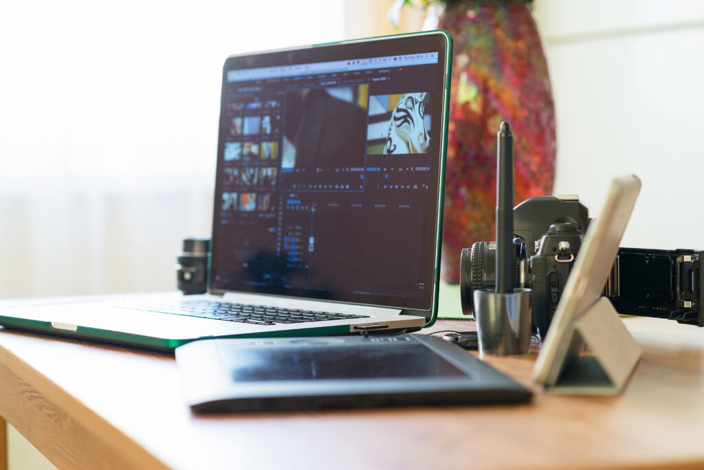 Work space or desktop hipster photographer in the sunlight from the window. Laptop, film camera, film roll, tablet and several lenses on a wooden table.